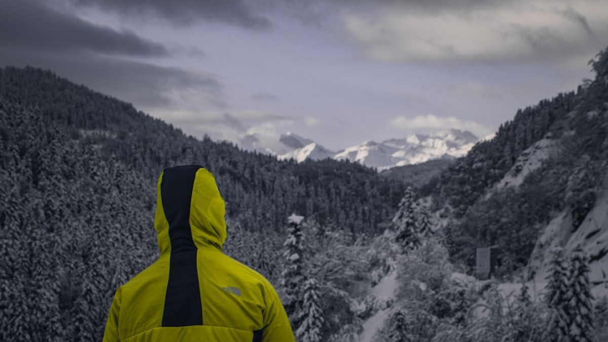 a man in a yellow jacket looking at a snowy mountain